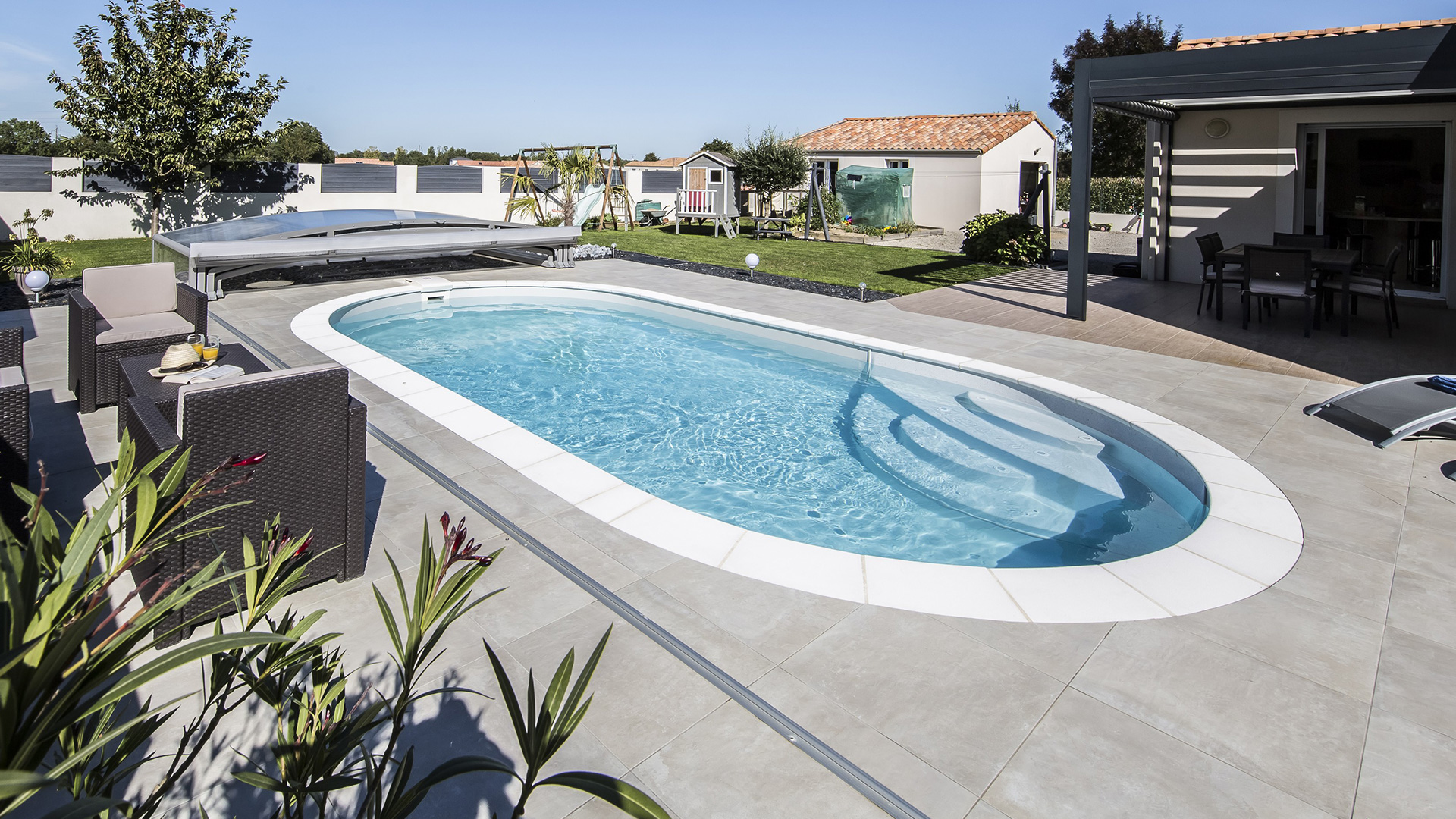 Piscine ovale Elsa dans un jardin avec terrasse en dalles de béton