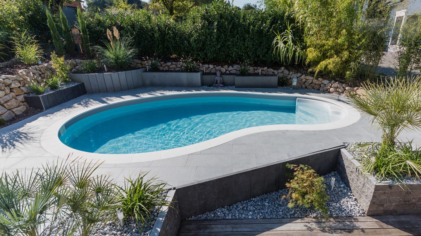 Aménagement jardin piscine enterrée forme haricot plage dalles de béton