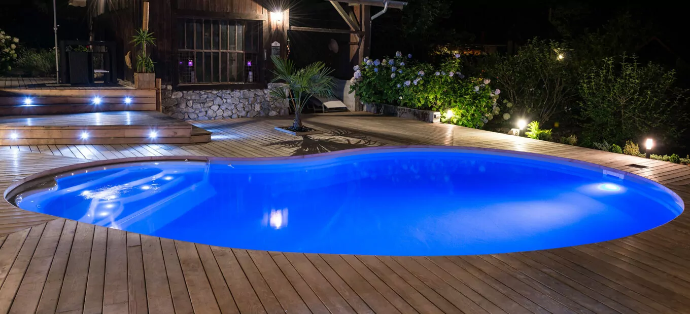 Superbe piscine Waterair en forme de haricot éclairée par des projecteurs