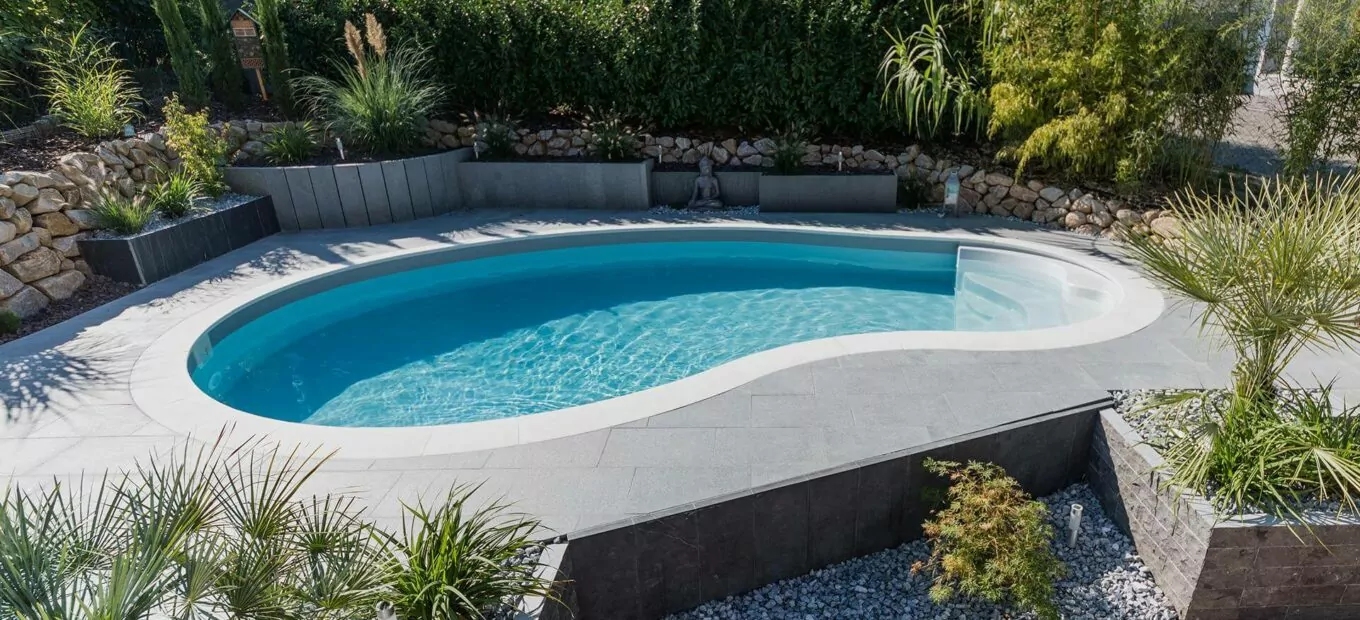 Giardino con piscina interrata a forma di fagiolo con area a bordo vasca in lastre di cemento